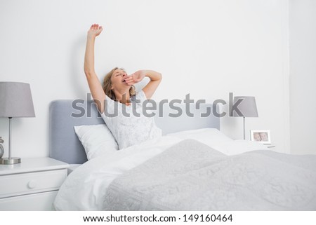 Blonde woman stretching and yawning in bed in the morning in bedroom at home