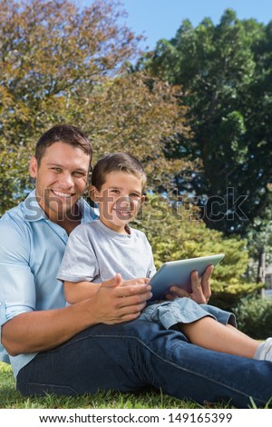 Dad and son with a tablet pc smiling into the camera in a park