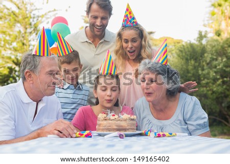 Happy extended family blowing out birthday candles together outside in the park