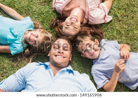 Happy family lying on the grass in a circle smiling at camera in park