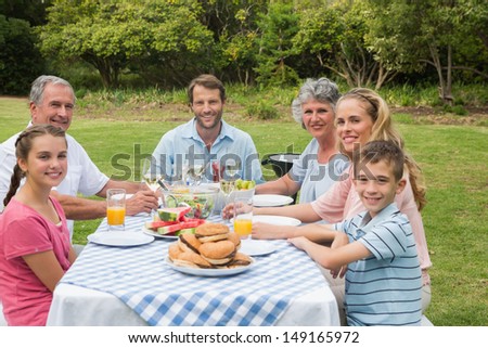 Multi generation family having dinner outside at picnic table smiling at the camera