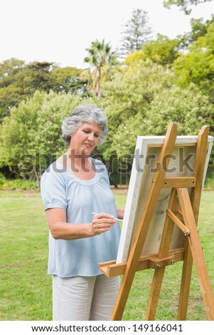Happy retired woman painting on canvas in park