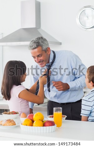 Daughter fixing her fathers tie with son in the kitchen at home in the morning