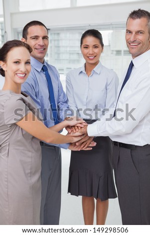 Smiling work team joining hands together in bright office