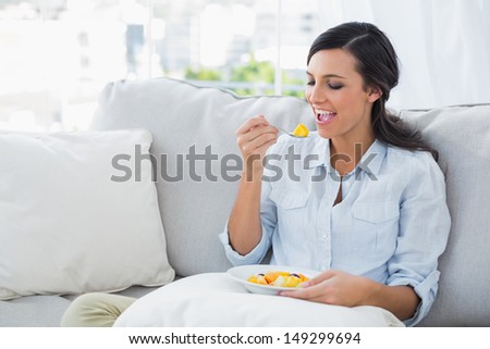 Woman relaxing on the sofa eating fruits salad in her living room