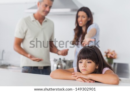 Couple having dispute in front of their upset daughter sitting in kitchen at home