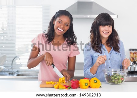 Happy friends preparing a salad together at home in kitchen smiling at camera