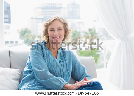 Content blonde woman sitting on her couch smiling at camera at home in the sitting room