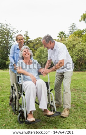 Retired woman in wheelchair with husband and daughter laughing in the park