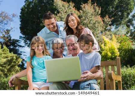 Smiling multi generation family with a laptop sitting in park on a bench