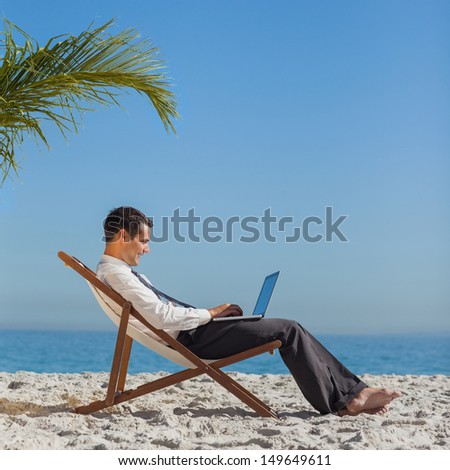 Young businessman relaxing on his beach chair using his laptop