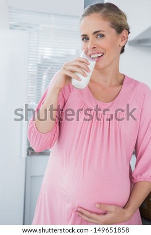Happy expecting woman in her kitchen drinking milk
