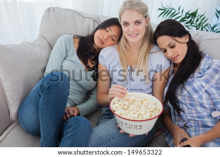 Friends dozing on blonde friends shoulders eating popcorn at home on couch