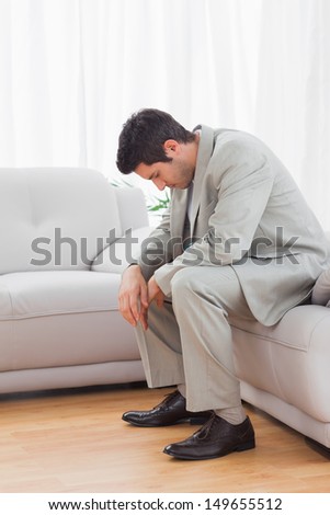 Troubled businessman sitting on sofa lowering his head at office