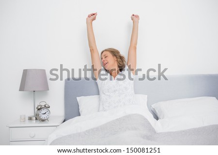 Well rested blonde woman stretching after waking up in bed in bedroom at home