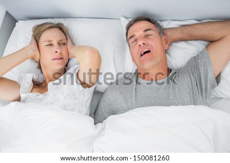 Annoyed Wife Blocking Her Ears From Noise Of Husband Snoring In Bedroom At Home