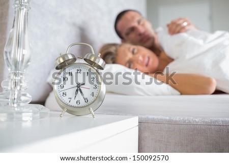 Exhausted couple looking at alarm clock  at home in bedroom