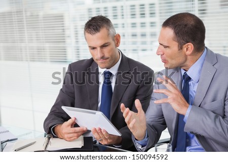 Serious businessmen analyzing documents on their tablet in bright office