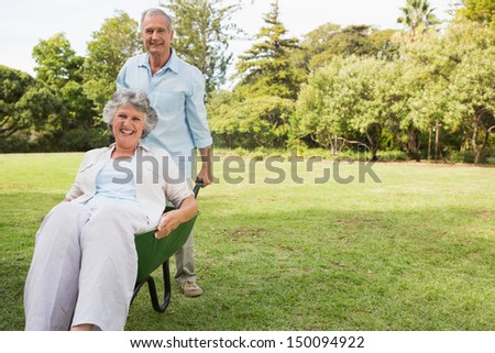 Happy man pushing his wife in a wheelbarrow outside in the sunshine