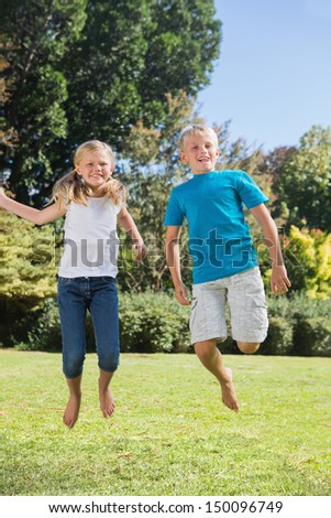 Brother and sister jumping together in the park on summers day