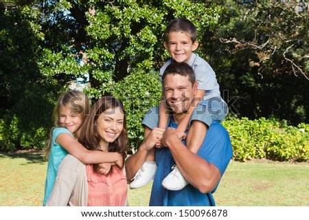 Young family with two children standing together in a park smiling at camera