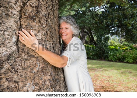 Smiling older woman hugging a tree in a park