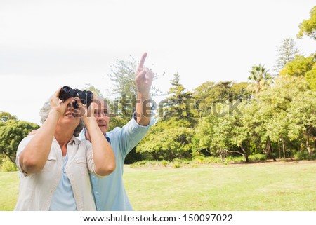 Man showing something to his wife with binoculars in the park on sunny day