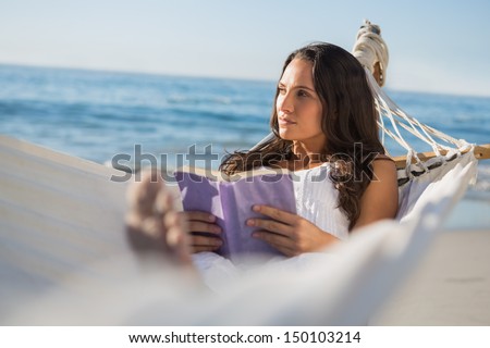 Woman lying on hammock holding book and thinking on the beach