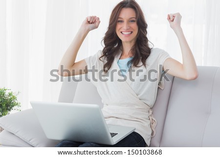 Cheering woman with laptop on her knees and sitting on the couch