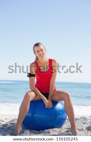 Fit woman sitting on exercise ball smiling at camera on the beach