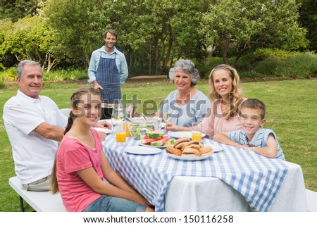 Happy extended family having a barbecue being cooked by father looking at camera