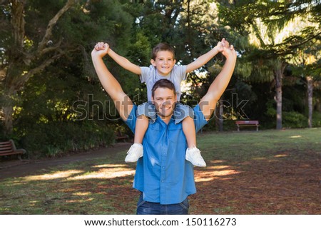 Father holding his son on shoulders and stretching out their arms in the park