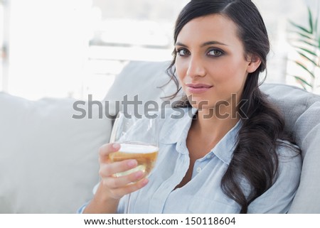 Pretty brunette drinking white wine sitting on sofa in her living room