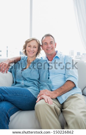 Middle aged couple sitting on the couch smiling at camera at home in the living room