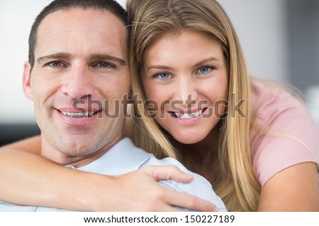 Woman hugging her partner from behind smiling at camera in sitting room at home