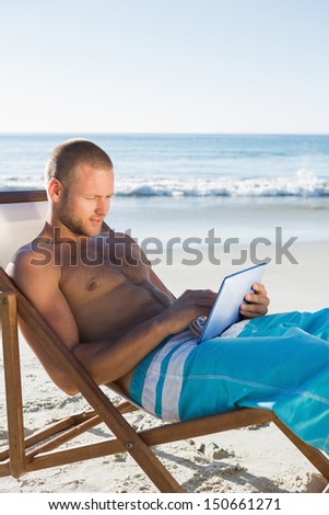 Concentrated handsome man on the beach using his tablet while sunbathing