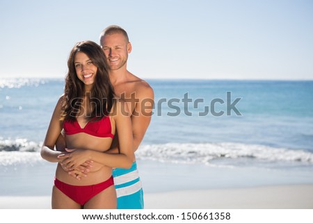 Loving couple on the beach embracing one another while looking at camera