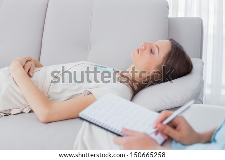Pensive woman lying on the couch while psychologist writing and advising her