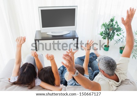 Family raising their arms in front of television at home