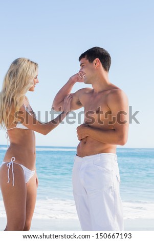 Handsome man showing off muscles to pretty blonde at the beach