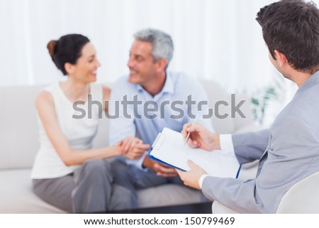 Couple speaking while salesman is holding contract on couch at home