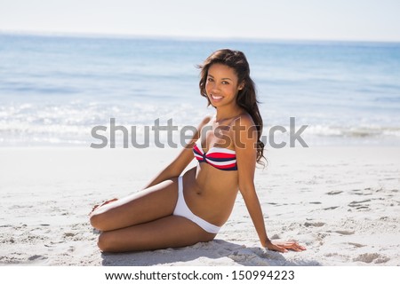 Sexy tanned woman in bikini smiling at camera while posing on the beach
