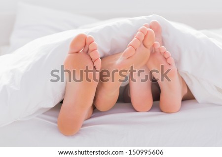 Couple rubbing their feet together under the duvet in bed