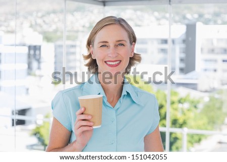 Businesswoman holding disposable coffee cup smiling at camera