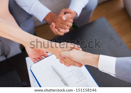 Salesman shaking hand with client with contract on the coffee table