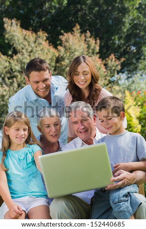 Multi generation family with a laptop sitting in park on a bench and smiling