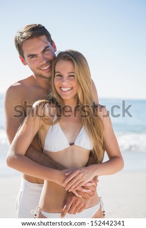 Happy couple smiling at camera and hugging on the beach
