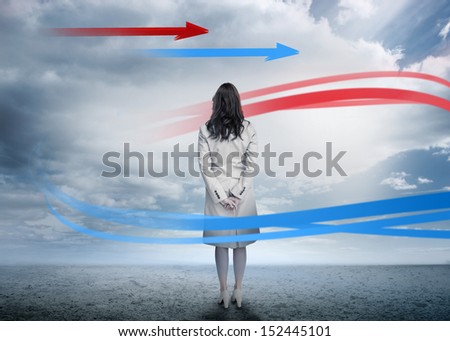 Businesswoman looking at red and blue arrows in cloudy desert landscape