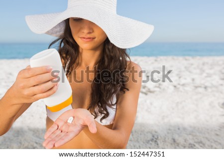 Sexy young brunette on the beach taking care of her body putting on sun cream