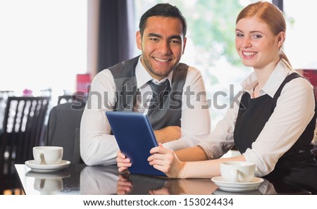 Business team working on tablet pc together in a cafe smiling at camera